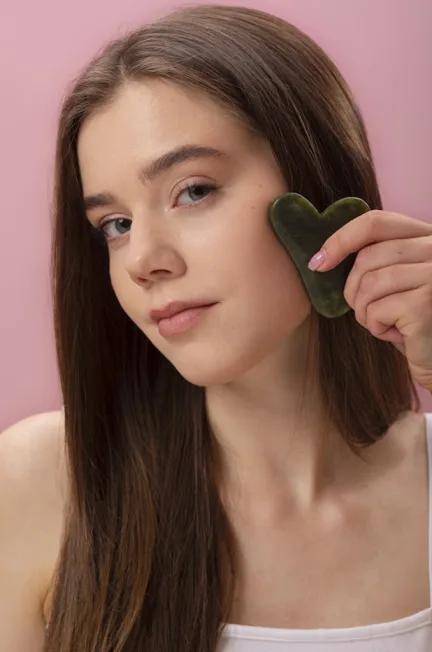 A young woman uses a gua sha tool to massage her face, promoting relaxation and improving circulation.